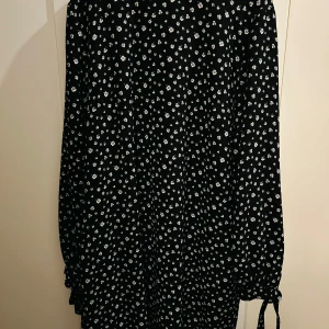 Svart, vit, begie och grön blommig klänning från H&M - Säljer en superfin svart klänning från H&M med små vita, gröna och begiea blommor. Den har långa ärmar och en bekväm passform, perfekt för både vardag och fest. Klänningen är i storlek XL och har en söt knytning vid ärmsluten. Ett måste i garderoben för alla säsonger!
