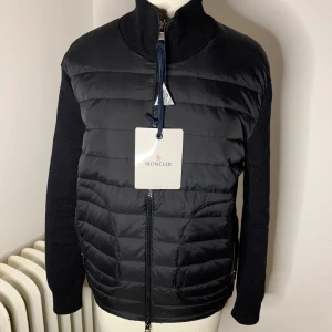 Moncler cardigan  - Säljer en snygg svart jacka från Moncler. Den har en quiltad framsida med dragkedja och långa ärmar. Perfekt för höst och vår! Jackan är i nyskick och har en stilren design med Moncler-logga på ärmen.