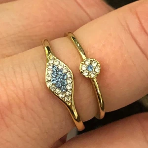Två söta Guld ringar  - En ring med liten blomma i vitt och baby blå strass diamanter guld metall  Och en ring med stenar i vitt och blått  Dem passar fint tillsammans  Inte använda pga fel storlek nickelfria 