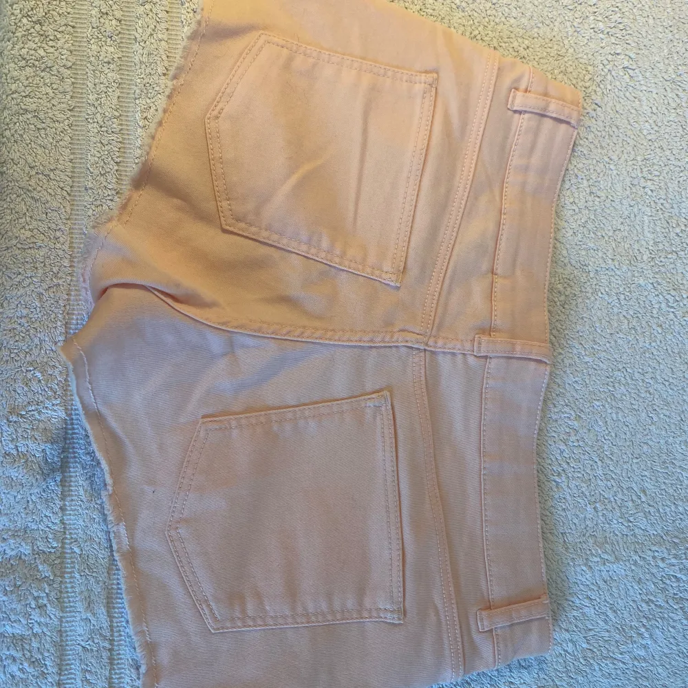 Säljer ett par ljusrosa shorts från H&M Divided i storlek 38. De är i bomull och har en snygg fransig kant nedtill. Perfekta för sommardagar och har en bekväm passform med låg midja. Använda men i bra skick!. Shorts.