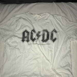 Vit AC/DC t-shirt - Säljer en vit AC/DC t-shirt med trycket 'Let There Be Rock 1977'. (St XL men skulle säga M) Pris kan diskuteras 