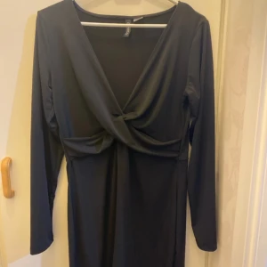 Svart klänning från H&M - Snygg svart klänning från H&M i storlek L. Den har en elegant omlott-design framtill och långa ärmar, perfekt för höst och vinter. Klänningen är i ett mjukt och bekvämt material, vilket gör den idealisk för både fest och vardag.