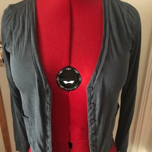 Grå kofta från H&M - Säljer en stilren grå kofta från H&M i storlek S. Den har långa ärmar och knappar framtill, perfekt för lager-på-lager under hösten. Materialet är mjukt och bekvämt, vilket gör den idealisk för både vardag och kontor. Ett måste i garderoben! 🌟