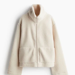 Beige teddyjacka med dragkedja - Mysig beige teddyjacka perfekt för kyliga dagar. Den har en dragkedja framtill och stora fickor för extra komfort. Jackan är långärmad och har en hög krage som håller dig varm. Perfekt för höst och vinter!