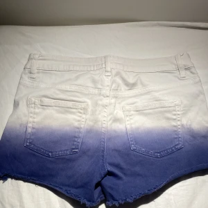 Blå och vita shorts med ombre-effekt - Sjukt snygga  shorts med en cool ombre-effekt från vitt till blått. De har en knapp med texten 'Young Forever' och en dragkedja framtill.