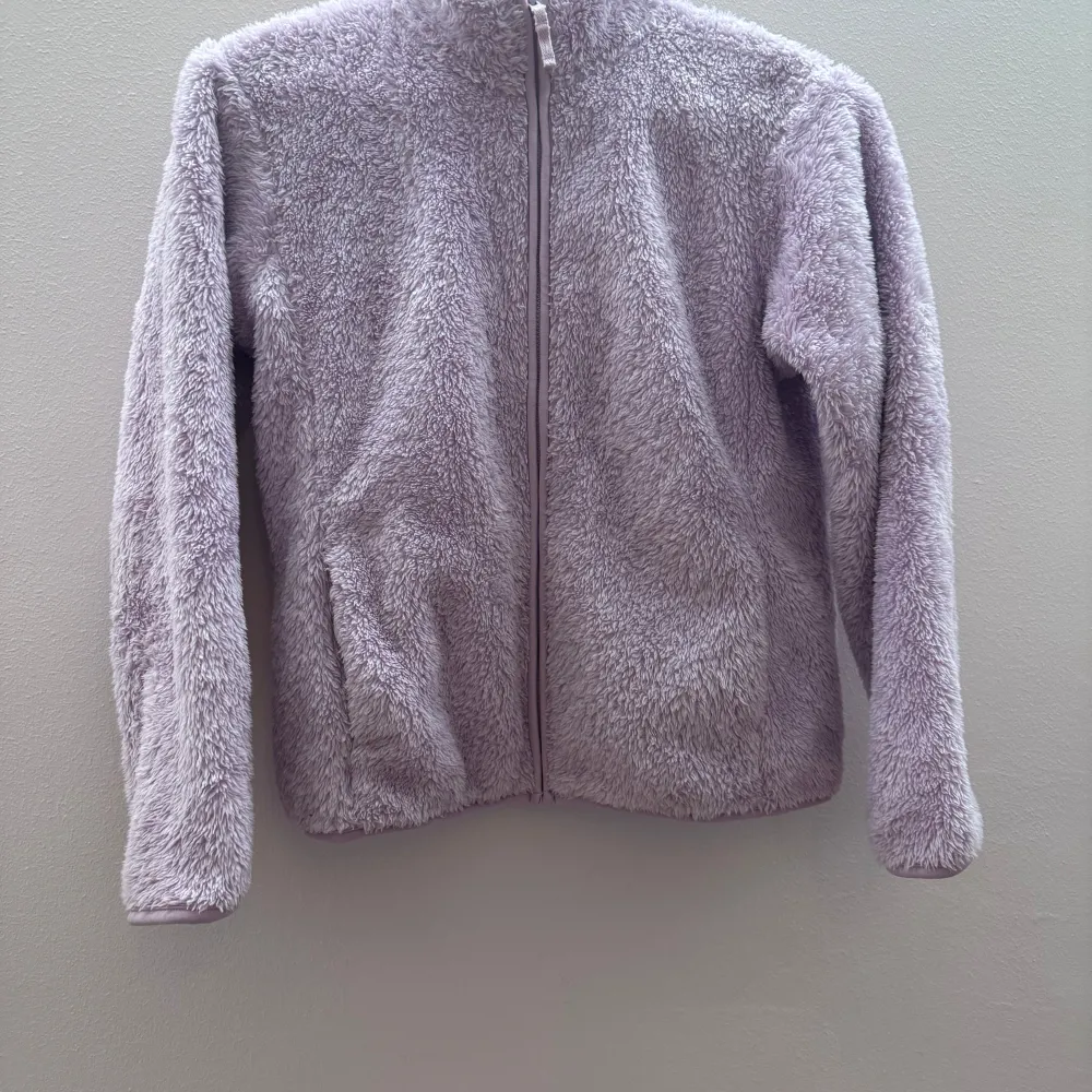 Mysig lila teddyjacka med dragkedja framtill. Perfekt för kyliga dagar med sin fluffiga och mjuka textur. Jackan har långa ärmar och en enkel design som gör den lätt att matcha med olika outfits.. Takit.