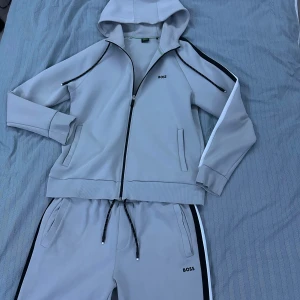 Tracksuit från Boss - Snygg grå Tracksuit från Boss. Den har svarta och vita detaljer längs ärmarna och benen med en diskret logga på bröstet och byxan! Perfekt för en avslappnad stil. Nypris 3600kr och de är knappt använd‼️