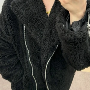 Svart teddyjacka från NA-KD - Mysig svart teddyjacka från NA-KD med dragkedja framtill. Perfekt för kyliga dagar med sin fluffiga och varma design. Jackan har långa ärmar och en avslappnad passform.