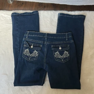 Blå bootcut jeans med broderade fickor - Snygga blå bootcut jeans med dekorativa broderier på bakfickorna. De är mid Waist i storlek Small.