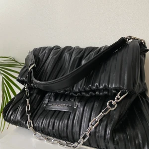 Svart axelväska från Karl Lagerfeld - Har inga tecken på användning men då den har nått åt på sig säljer jag den billigare. Nypris ca 2 500kr. Karl Lagerfeld hopvikt väska i mjukt plisserat tekniskt läder, justerbar och avtagbar axelrem i läder och en avtagbar axelrem på kedjan, magnetisk stängning, invändig ficka med dragkedja samt bakficka Höjd 25-30 beroende på uträckt eller ihopvikt Längd ca 30-34 cm 