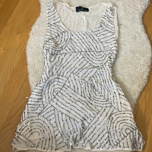 Vit glittrigt linne/klänning  - Säljer en snygg vit kortklänning/ linne med glittriga paljettdetaljer i ett geometriskt mönster. Perfekt för en festlig kväll! ✨