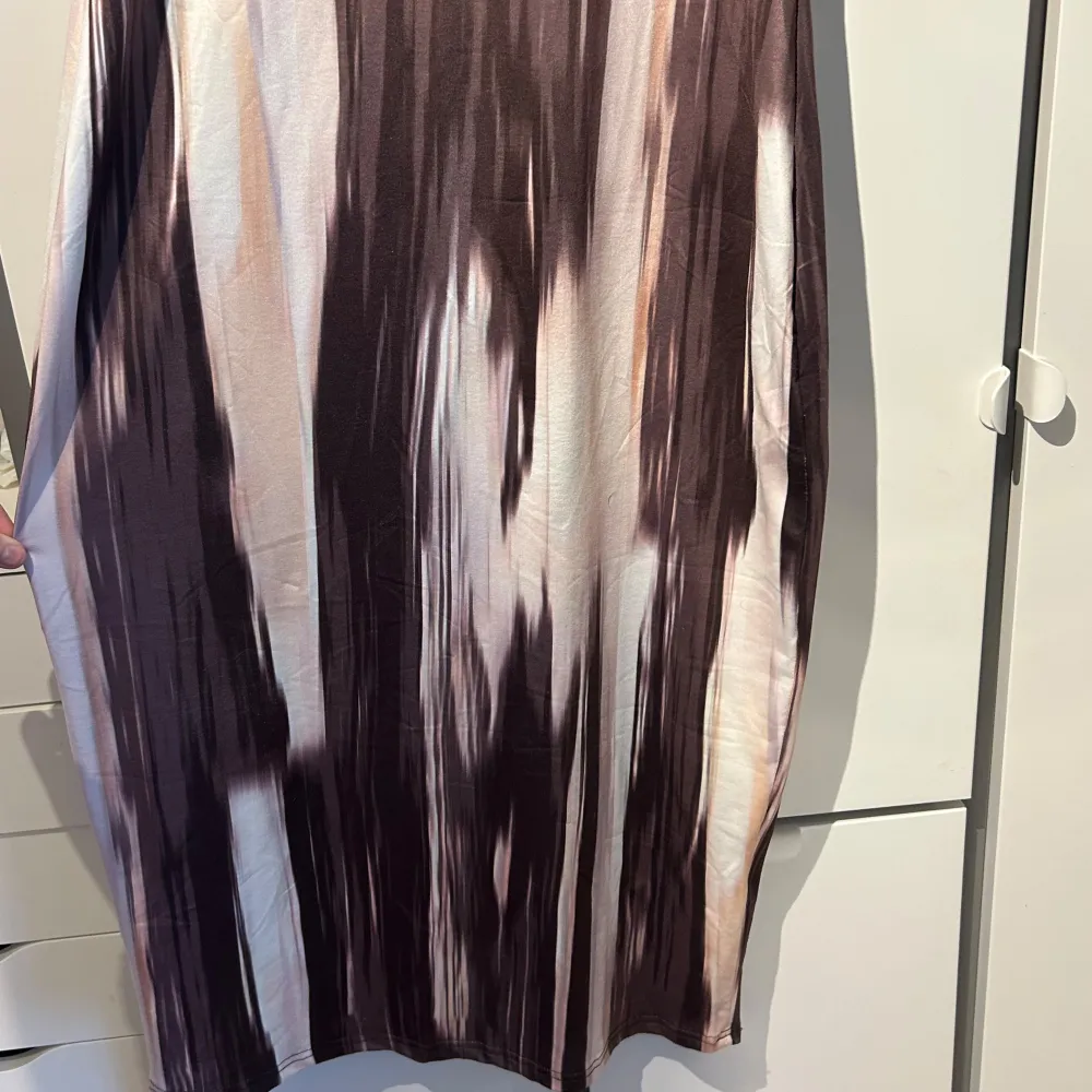 Säljer en cool ärmlös klänning med ett abstrakt mönster i bruna och beige toner. Klänningen har en lång passform och rund halsring. Mekot.