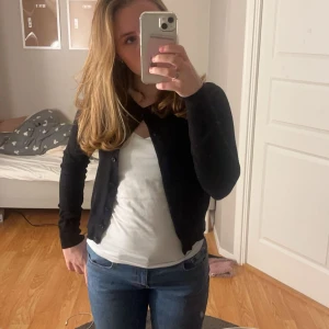 Svart kofta från H&M - Säljer en klassisk svart kofta från H&M i storlek XS. Koftan har långa ärmar och knappar framtill, perfekt för lager-på-lager-stil. En mångsidig basplagg för garderoben.