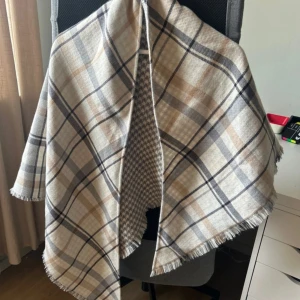 Rutig halsduk från s.Oliver - Snygg och stilren halsduk från s.Oliver med ett klassiskt rutigt mönster i beige, grå och svart. Den har en mjuk och skön känsla, perfekt för kyliga dagar. Fransen ger en extra touch av stil.