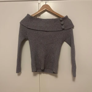 Grå ribbad tröja från Oxygene - Säljer en stilren grå ribbad tröja från Oxygene med en bred krage och dekorativa knappar. Tröjan har långa ärmar och en bekväm passform. Perfekt för kyligare dagar.