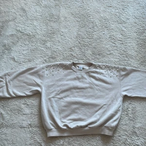 Beige tröja från Lindex Kids - Säljer en beige tröja från Lindex Kids i storlek 146/152. Tröjan har långa ärmar och dekorativa pärlor på axlarna. Passar barn i åldern 10-12 år.