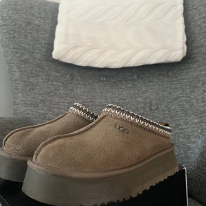 Bruna mocka slip-ons från UGG - Snygga bruna slip-ons från UGG i mocka med dekorativ kant. Skorna har en robust sula och är perfekta för en avslappnad stil. De är bekväma och lätta att ta på. 