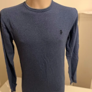 Blå tröja från U.S. Polo Assn. - Säljer en stilren blå tröja från U.S. Polo Assn. med rund hals och broderad logga på bröstet. Tröjan har långa ärmar och en slim fit passform, perfekt för en snygg och bekväm look.