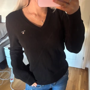 Svart tröja från GANT - Säljer en jättefin svart tröja från GANT med v-ringning. Tröjan är i storlek M men passar även mig som har storlek XS beroende på hur man vill ha passformen. Tröjan är 100% bomull och i väldigt fint skick.