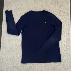Mörkblå tröja från Lyle & Scott - Säljer en stilren mörkblå tröja från Lyle & Scott med deras ikoniska gula logotyp på bröstet. Tröjan har långa ärmar och är perfekt för en avslappnad stil. Passar ungdomar i åldern 14-15 år.