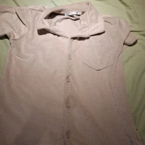 Beige frottéskjorta med kort ärm - Säljer en beige frottéskjorta med korta ärmar och knappar framtill. Skjortan har en klassisk krage och en bröstficka. Perfekt för en avslappnad stil.