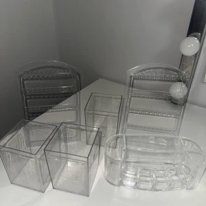 Transparenta sminkförvaringslådor - Säljer ett set med transparenta sminkförvaringslådor i olika storlekar och former. Perfekt för att organisera smink som läppstift, borstar och andra småsaker. Tillverkade i klar plast för enkel överblick och stilren förvaring på sminkbordet. Nya sminkställ. Ingen synlig skada bara behövs damas av. Öre hänge hållare Pris kan diskuteras😘