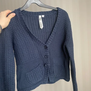 Mörkblå stickad kofta från E.B. Design - Säljer en mörkblå stickad kofta från E.B. Design. Koftan har en v-ringning och knappar framtill samt två fickor. Den är aldrig använd