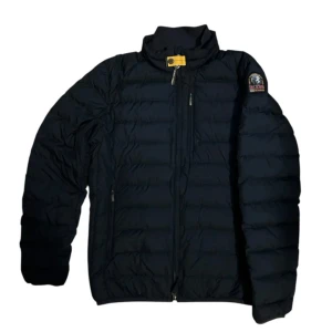Parajumpers - Säljer en svart dunjacka från Parajumpers med en snygg patch på ärmen. Jackan har en dragkedja framtill och är superlätt, perfekt för kyliga dagar. Den har en hög krage och är designad för att hålla dig varm och bekväm.