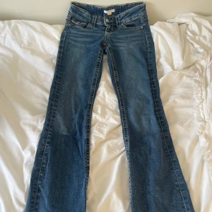 Blå bootcut jeans - Snygga blå bootcut jeans med klassisk femficksdesign och knappar på bakfickorna. De har en lågmidjad passform och är tillverkade i jeansmaterial. Jeansen är från Gina Tricot Young och är använda ett fåtal gånger. Storlek 158. 
