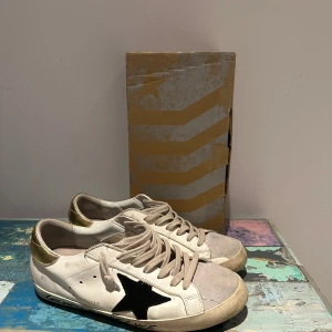 Golden Goose Superstar sneakers - Snygga Golden Goose Superstar sneakers i vitt med svart stjärna och guld på hälen. Skorna är knappt använda, vilket man kan se på sulan eftersom att den slits lätt. Säljer skorna eftersom att de var för små. Tar emot byten mot Maison Margielas i storlek 44-45