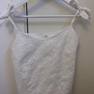 Vit broderad linnetopp - Söt vit linnetopp med broderade blommor och knytband vid axlarna. Den är inte genomskinlig. Meddela mig om det är några minsta funderingar💕