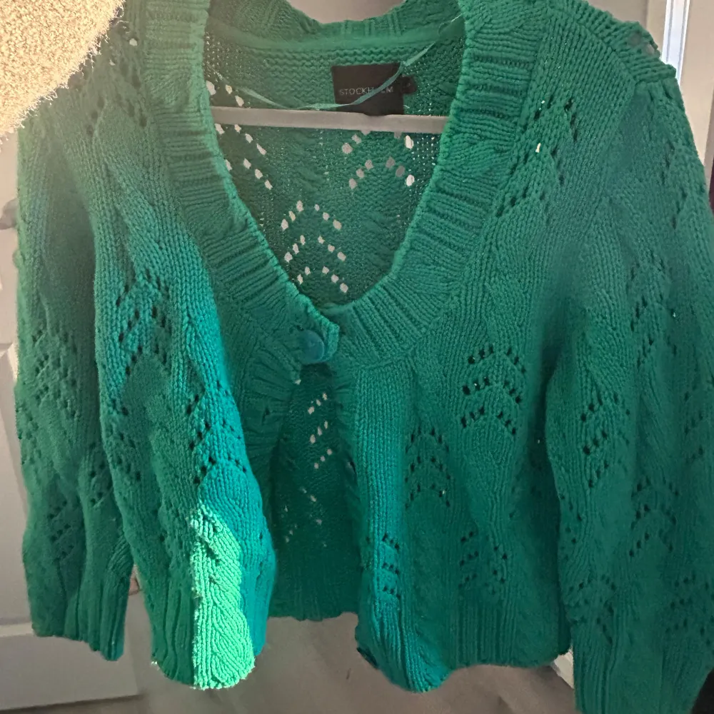 Säljer en snygg grön stickad kofta från Stockh lm. Koftan har ett fint hålmönster och knappar framtill. Perfekt för att lägga till en färgklick i garderoben. Passar bra till både jeans och kjol.. Neuletakit & Villapaidat.
