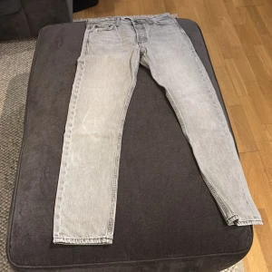 Grå jeansbyxor från Jack and Jones - Snygga grå jeansbyxor med en klassisk straight passform. De har en midwaist design och är perfekta för en avslappnad stil. Byxorna har fem fickor och en dragkedja framtill.