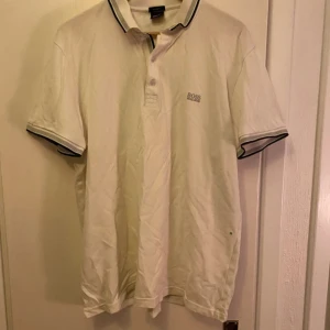 Vit kortärmad pikétröja från Hugo Boss - Säljer en stilren vit pikétröja från Hugo Boss med korta ärmar och klassisk krage. Tröjan har en broderad logga på bröstet och kontrastfärgade detaljer vid krage och ärmslut. Perfekt för en avslappnad men ändå elegant look. Storlek xxxl men passar mera som en xl!