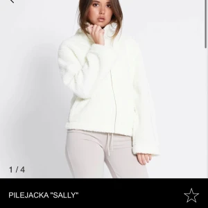 Vit pilejacka 'Sally' - Mysig vit pilejacka med dragkedja och hög krage. Perfekt för kyliga dagar med sin fluffiga och varma design. Jackan har en avslappnad passform och långa ärmar. 