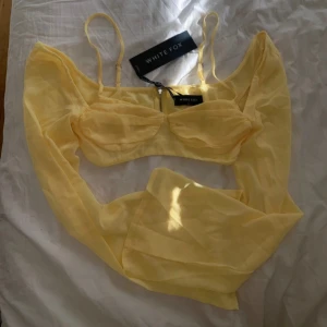 Gul topp från White Fox - Säljer en snygg gul topp från White Fox med transparenta långa ärmar och justerbara axelband. Toppen har en dragkedja framtill och en stilren design som passar perfekt för varmare dagar.