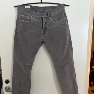 Grå manchesterbyxor - Snygga grå manchesterbyxor med klassisk design. Byxorna har en normal passform och är perfekta för en stilren look. De har både knappar och dragkedja framtill. Storlek 31/32