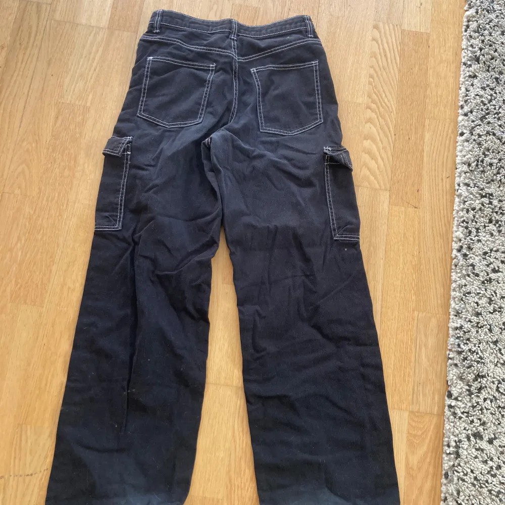 Säljer ett par svarta cargopants från H&M Divided i storlek 36. Byxorna har en loose passform och är tillverkade i bomull. De har flera praktiska fickor på sidorna och bak, samt vita sömmar som ger en snygg kontrast. Perfekta för en avslappnad och cool stil!. Farkut & Housut.