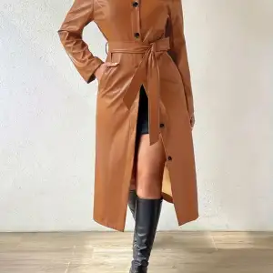 Säljer en snygg brun trenchcoat i syntetmaterial. Jackan har en klassisk design med knappar framtill och ett bälte i midjan för en figursydd passform. Den är långärmad och perfekt för höst- och vårsäsongen. Jackan är i nyskick och har en normal passning. Ha två storlekar man kan beställa (m & s) 