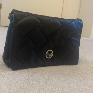 Svart quiltad axelväska från NYPD - Säljer en snygg svart quiltad axelväska från NYPD (New York Portable Design). Väskan har en elegant design med ett flätat mönster och en kedjerem med en bekväm axelvaddering. Den har en dragkedja på insidan för extra säkerhet och ett stilrent metallmärke på framsidan. Perfekt för både vardag och fest! den har dock rostat lite på kedjan och det ser ni på sista bilden. super snygg väska🫶🏼