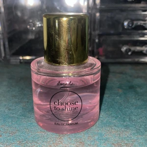 Choose to Shine Eau de Parfum - Säljer en superfin parfym från  ILivande som heter 'Choose to Shine'. Flaskan är rund och genomskinlig med en ljusrosa vätska inuti. Den har en elegant guldig kork som ger en lyxig känsla. Perfekt för att ge en fräsch och blommig doft hela dagen. Köp den nu och lys upp din dag! 🌸✨