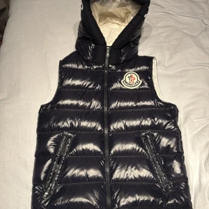 Mörk blå dunväst från Moncler Barn Storlek - Säljer en snygg till 14 åringar, då moncler använder anni när det kommer till barn storlekar. varm svart dunväst från Moncler. Västen har en huva och dragkedja framtill. Perfekt för höst och vinter! Inprincip ny skick, använt ett par gånger! 🖤