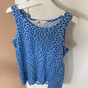 Blå blommig ärmlös topp från H&M - Säljer en söt blå ärmlös topp från H&M med ett blommigt mönster. Toppen är perfekt för sommaren och är i ett mjukt och bekvämt material. Passar bra till både jeans och kjol. Köp direkt eller ge prisförslag 💙köparen betalar för frakt 