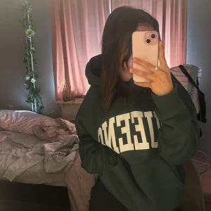 Mörkgrön hoodie från Pull&Bear - Säljer en mörkgrön hoodie från Pull&Bear i storlek S. Den är supermysig och perfekt för höst och vinter. Hoodien har en stor vit text på framsidan och en klassisk känguruficka. Den är i nyskick och väldigt bekväm att ha på sig. Perfekt för en chill dag hemma eller en promenad i parken.