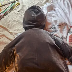 Säljer en mörkgrå hoodie med dragkedja framtill. Den är tillverkad i ett mjukt och glansigt material, vilket gör den både bekväm och stilren. Hoodien har en luva och elastiska muddar vid ärmslut och nederkant. Perfekt för en avslappnad och cool look! ⚠️modellen är en docka⚠️