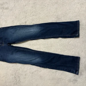 Blå jeans från Emporio Armani - Snygga blå jeans från Emporio Armani med klassisk design. De har en knapp med märkets logga och en läderdetalj baktill. Perfekta för en stilren look.