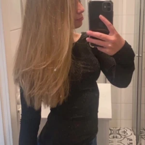 Svart glittrig topp - Snygg svart glittrig topp med långärmad design och öppen rygg. Perfekt för en kväll ute eller en festlig tillställning. Toppen har en tight passform som framhäver figuren.