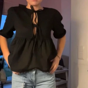 Svart blus med knytning - Snygg svart blus med knytning framtill och trekvartsärmar. Perfekt för en stilren look. från lager 157.