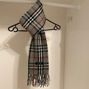 Burberry - Säljer nu denna Snygga halsduk från Burberry i färgen grå. Tillverkad i 100% kashmir med klassiskt fransad kant. Perfekt för att hålla dig varm och stilren under kyliga dagar. Hör av er vid funderingar☺️