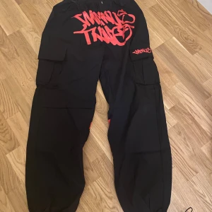 Minus twọ / Svarta cargopants med röd graffiti - Använda 4 gånger. Coola svarta cargopants med röd graffiti-design. Byxorna har flera fickor och elastiska muddar vid bensluten. Perfekta för en avslappnad streetwear-look.